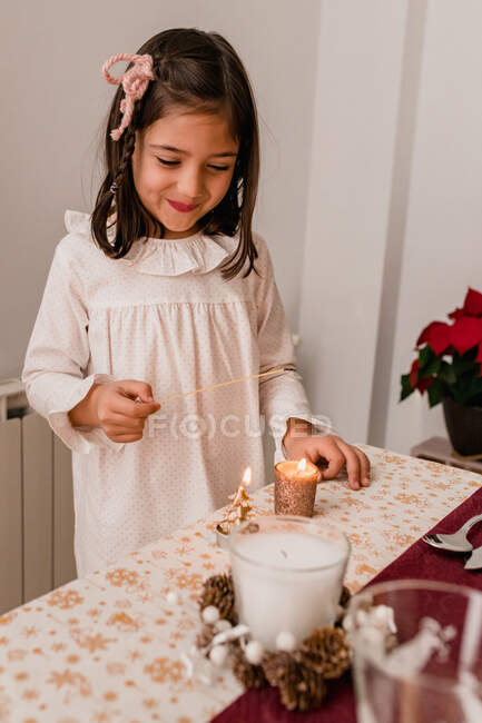 Cute girl in dress standing near festive table and lightning candles for celebrating Christmas holiday — Stock Photo