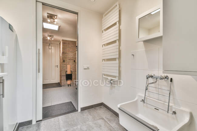 Contemporary bathroom with heated towel rail and washbasin against entrance door under lamp in house — Stock Photo