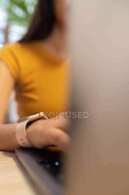 Обрізаний невпізнаваний молода жінка-підприємець сидить за столом і переглядає нетбук під час роботи на сучасному робочому місці — стокове фото