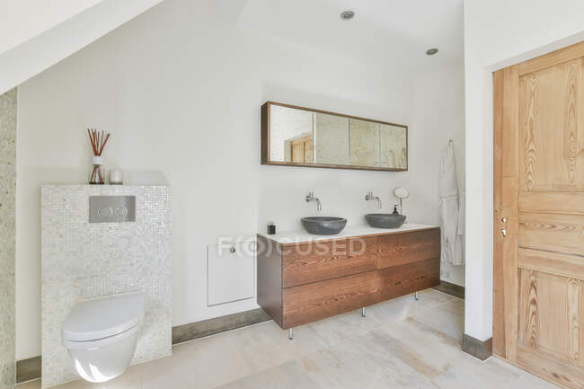 Interior do banheiro contemporâneo com paus de incenso na prateleira contra lavatórios entre armários e espelhos em casa de luz — Fotografia de Stock