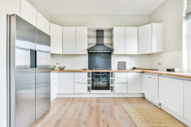 Ampia cucina luminosa con armadi bianchi e frigorifero vicino alla finestra — Foto stock