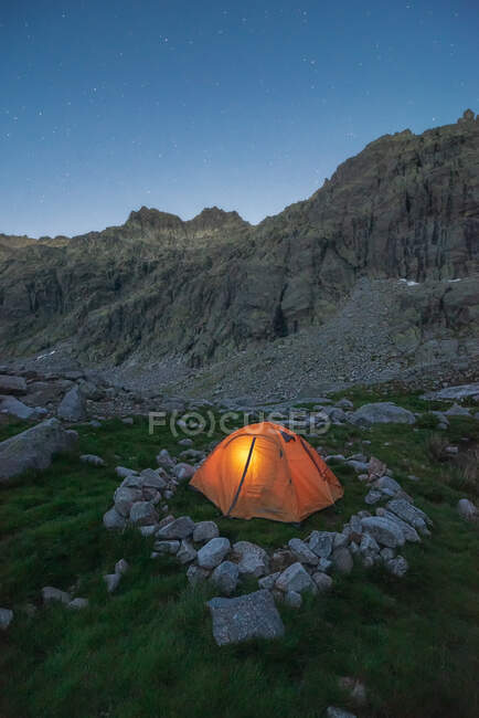 Vue pittoresque de la tente sur la mousse avec des pierres contre le mont accidenté sous le ciel bleu au crépuscule — Photo de stock