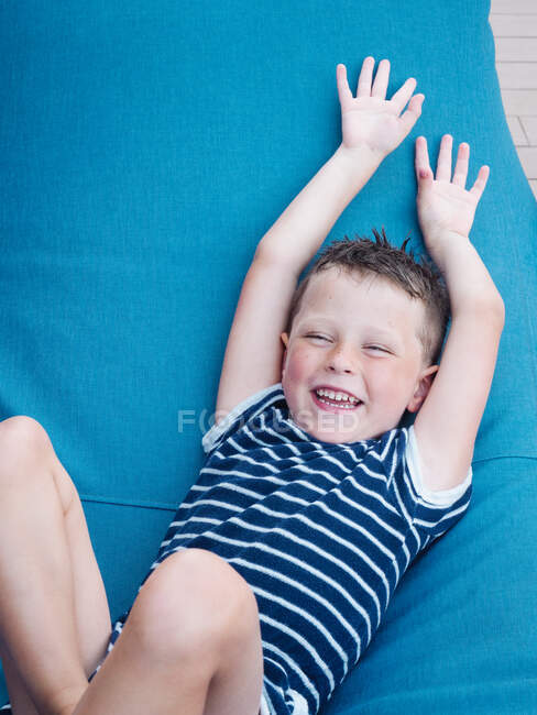 Alto ángulo de niño juguetón levantando brazos mientras monta en diapositiva y riendo felizmente - foto de stock