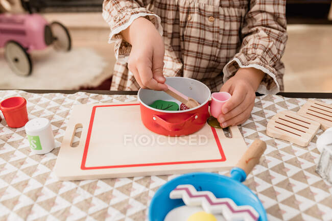 Niño atento en vestido a cuadros jugando con juguetes durante el proceso de cocción en la mesa en la sala de luz - foto de stock