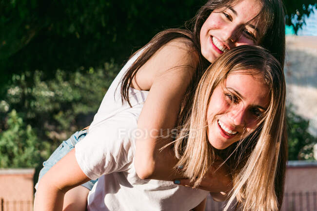 Веселий підліток дає врожай кращій подрузі-жінці їздити на полюванні, дивлячись на камеру в сонячному місті — стокове фото