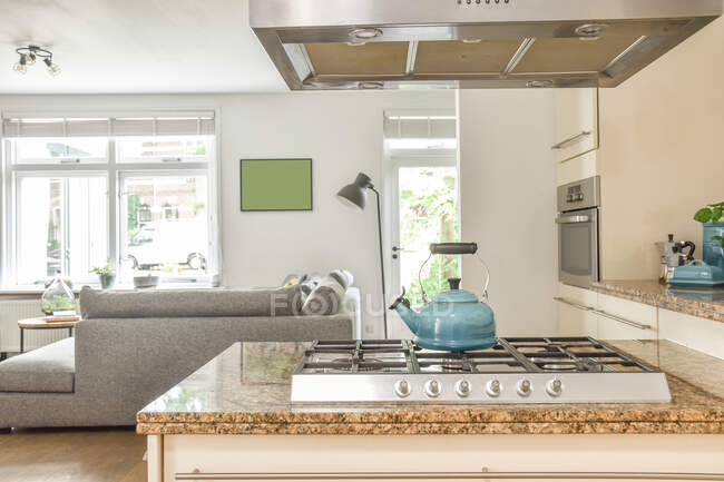 Hervidor de agua colocado en la estufa bajo ventilación en amplia cocina con muebles de luz en apartamento moderno - foto de stock