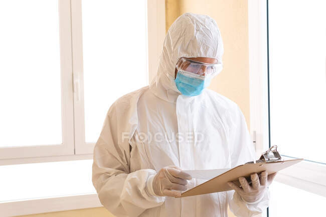 Medico adulto maschio in dispositivi di protezione individuale carta da lettura negli appunti durante la pandemia del COVID 19 in ospedale — Foto stock