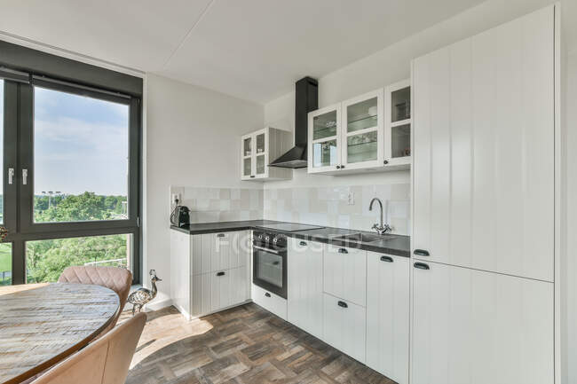 Стильный интерьер просторной кухни с белыми шкафами и кухней в современной квартире — стоковое фото