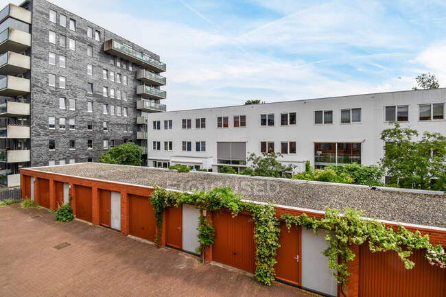 Moderne mehrstöckige Gebäude Außen und Garagen mit kriechenden Pflanzen gegen Gehweg unter bewölktem Himmel in Amsterdam Niederlande — Stockfoto
