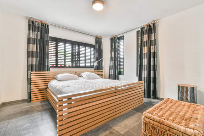 Современный интерьер спальни с кроватью с подушками под светящейся лампой на потолке в квартире — стоковое фото