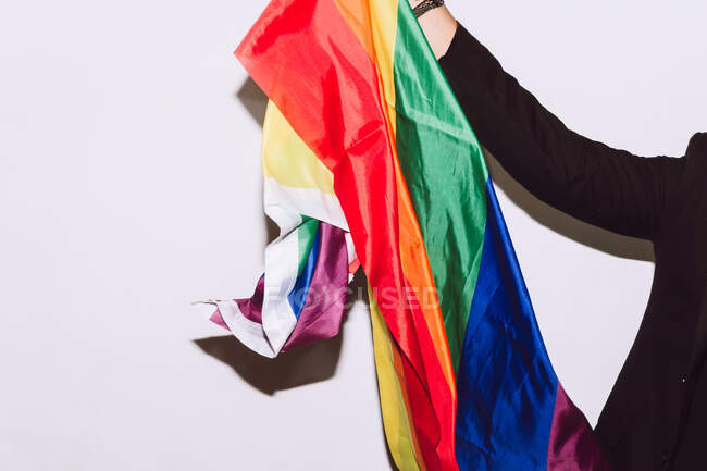 Cultivo irreconocible barbudo macho jugando y ondeando bandera multicolor símbolo del orgullo LGBTQ - foto de stock