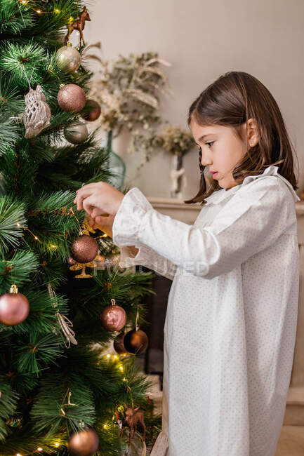 Side view of crop concentrated girl decorating Christmas tree branches while preparing home for holiday celebration — Stock Photo