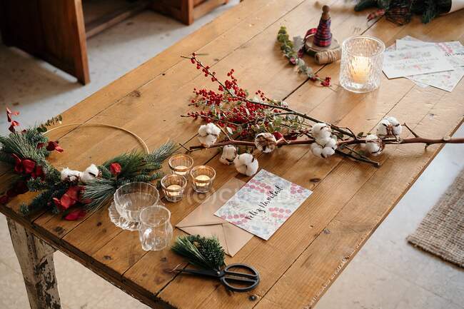 From above Christmas composition with colorful postcard with inscription Feliz Navidad placed near burning candles and cups of tea on wooden table decorated with colorful branches of plants — Stock Photo