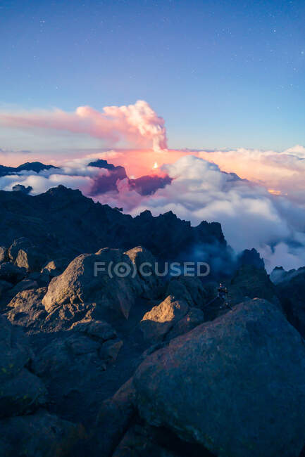 Night landscape with an erupting volcano in the background and a sea of clouds covering the mountains on a starry night from a vegetated and rocky mountain. Cumbre Vieja volcanic eruption in La Palma Canary Islands, Spain, 2021 — Stock Photo