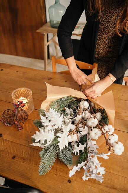 Crop unrecognizable female florist standing arranging Christmas bouquet on wooden table — Stock Photo