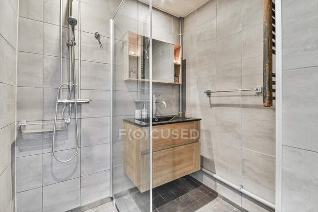 Интерьер современной ванной комнаты с душевой кабиной и раковиной выполнен в минимальном стиле с серой плиткой — стоковое фото