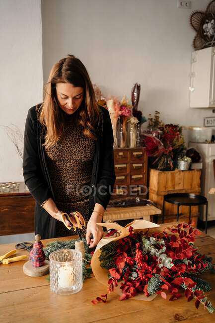 Calma florista femenina de pie en la mesa y la organización de ramo de flores en el estudio de floristería creativa - foto de stock