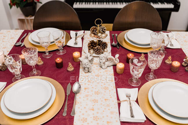 Сверху сервировка стола со стаканами и столовыми приборами рядом с тарелками, украшенными свечами и конусами для празднования Рождества — стоковое фото