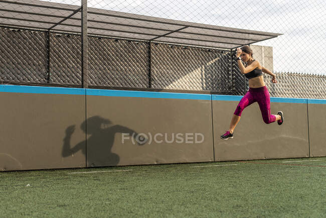 Corps entier d'athlète féminine durable en vêtements de sport sautant au-dessus du sol pendant l'entraînement intense dans le stade — Photo de stock