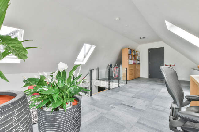 Intérieur gris de chambre spacieuse moderne au deuxième étage d'une grande maison décorée avec des plantes en pot près de la table et de la chaise — Photo de stock