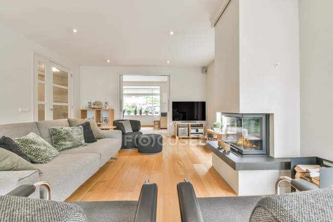 Quarto contemporâneo interior com poltronas e sofá com almofadas decorativas contra lareira em casa de luz — Fotografia de Stock