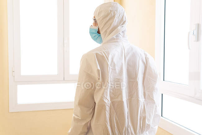 Vista posteriore del medico maschile irriconoscibile in dispositivi di protezione individuale con occhiali e maschera sterile in attesa contro la finestra in ospedale — Foto stock