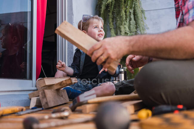 Ground level of cropped unrecognizable dad in checkered shirt with boy working with wooden blocks — Stock Photo