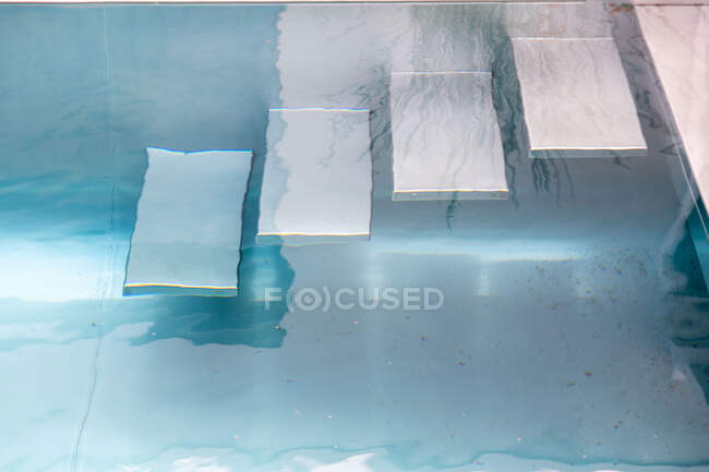 From above of stairs in swimming pool with transparent blue water in daylight — Stock Photo