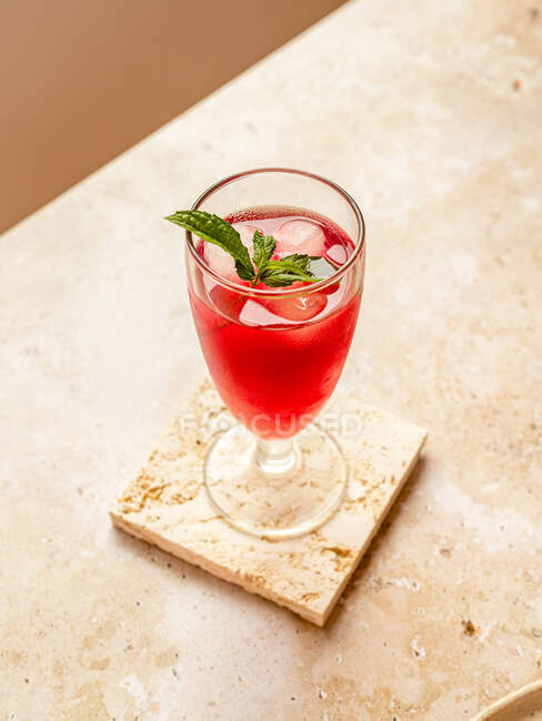 Dall'alto di bevanda rossa rinfrescante saporita con cubetti di ghiaccio e foglie di menta aromatiche in vetro su sottobicchiere — Foto stock