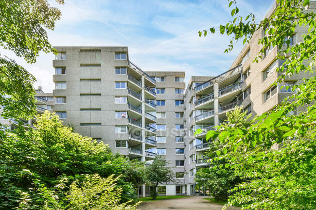 Fachada de concreto edifício residencial multiandares localizado no bairro da cidade com árvores verdes sob o céu azul — Fotografia de Stock