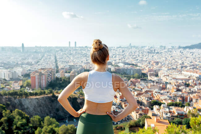 Vue arrière d'une athlète anonyme avec les mains sur la taille admirant la ville d'été au soleil — Photo de stock