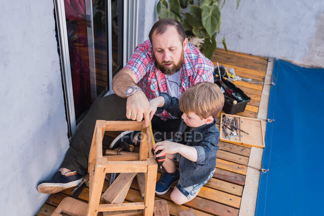 From above unshaven mature dad with attentive boy measuring wooden blocks with tape while spending time on blurred background — Stock Photo