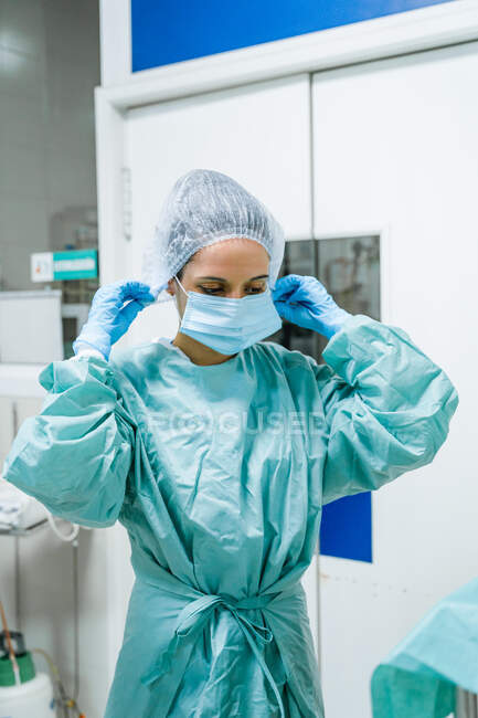 Young female veterinary surgeon in green uniform putting on disposable cap while looking forward in clinic — Stock Photo