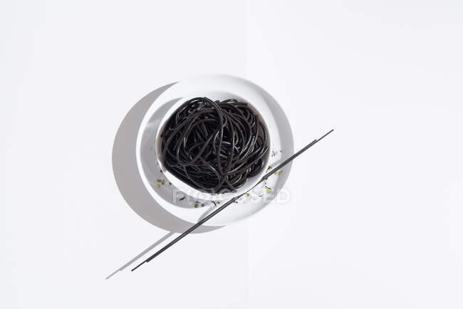 Du dessus du bol en céramique avec de délicieux spaghettis à l'encre de calmar noir avec des baguettes sur fond blanc — Photo de stock