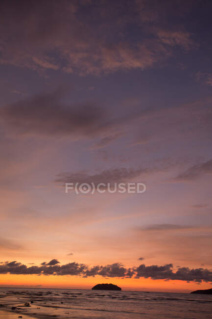 Вид на бесконечное море с холмами и волнами, катящимися по песчаному берегу под оранжевым закатом неба в Малайзии — стоковое фото