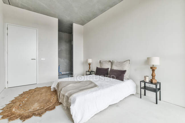 Kreative Gestaltung des Schlafzimmers mit Kissen und Bezug auf dem Bett zwischen Tür und Tischen auf dem Boden zu Hause — Stockfoto