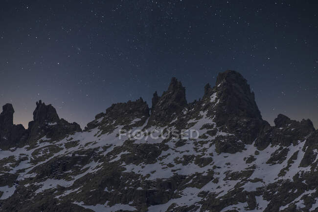 Vista panorâmica de montagens escuras com neve e picos ásperos sob o céu estrelado ao entardecer — Fotografia de Stock