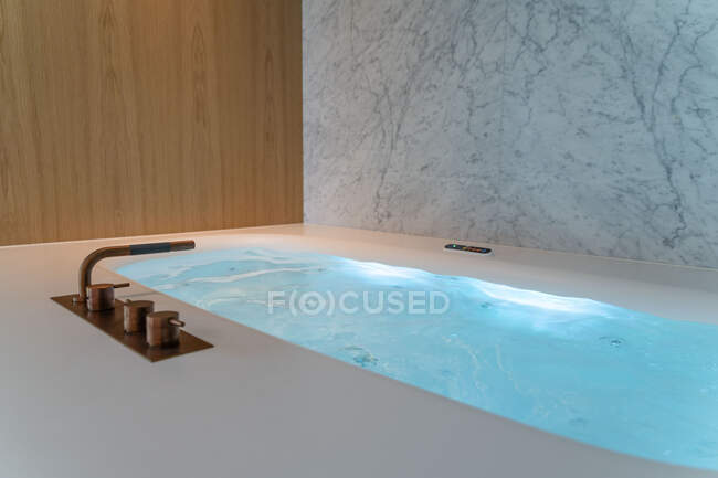 Інтер'єр сучасної ванної кімнати з гарячою ванною з чистою водою на тлі світлої стіни в квартирі — стокове фото