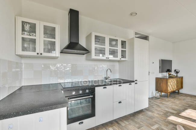 Стильный интерьер просторной кухни с белыми шкафами и кухней в современной квартире — стоковое фото