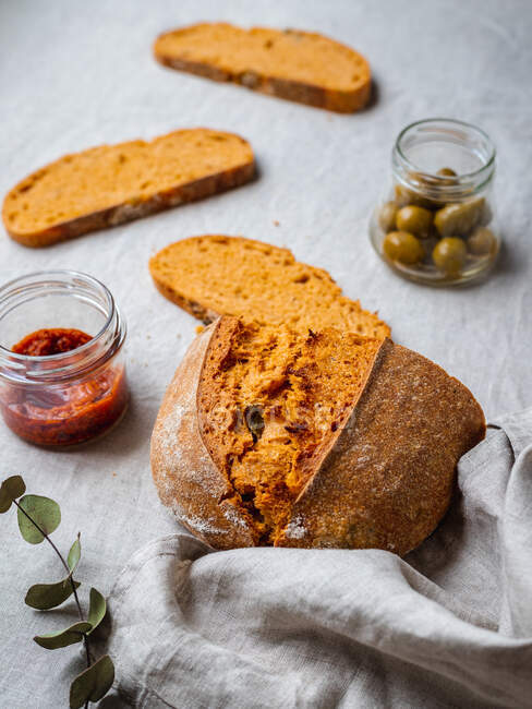 Dall'alto di pane di pane di taglio messo su tavolo vicino a salsa di pesto rossa e vaso di olive verdi — Foto stock