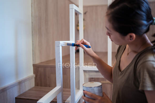 Vue latérale de jeune femme ethnique attentive avec cadre de balustrade de peinture au pinceau au-dessus des escaliers dans la maison — Photo de stock