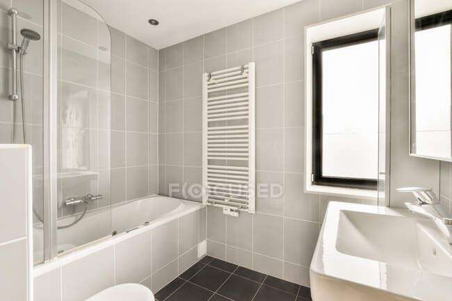 Bagno moderno interno con vasca contro finestra e lavabo sotto specchio in casa nella giornata di sole — Foto stock