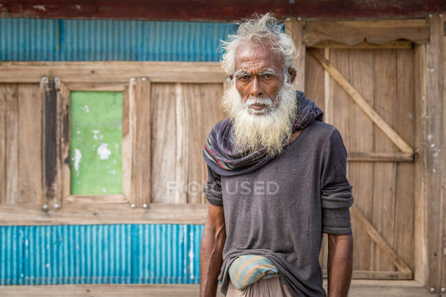 INDIA, BANGLADESH - DECEMBER 7, 2015: Senior ethnic male in traditional clothes looking at camera while standing on street of aged town — Stock Photo