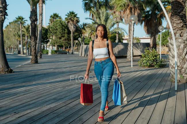 Joyeux jeune acheteur afro-américain avec des sacs à provisions regardant loin tout en marchant dans la rue — Photo de stock