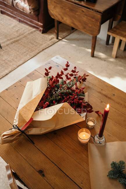 Сверху праздничный стильный декоративный рождественский букет с веточками эвкалипта и ярко-красными ветвями с ягодами, помещенными на деревянный стол со свечами в номере — стоковое фото