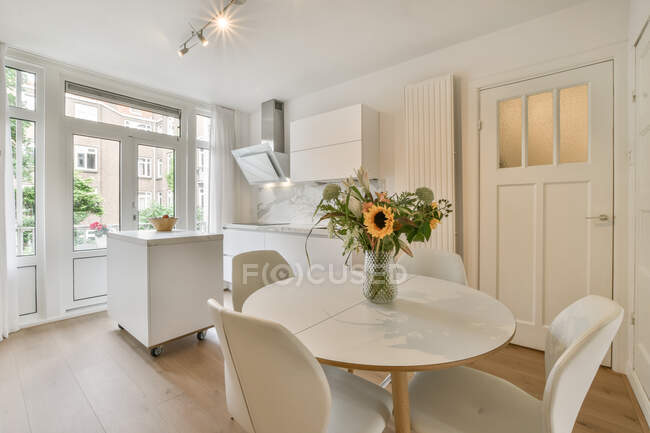Table ronde avec bouquet de fleurs placé près de la cuisine légère dans un appartement moderne en journée — Photo de stock