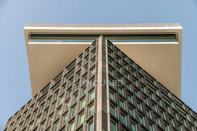 Из-под высокого многоэтажного здания с необычными окнами под голубым небом в современном городе — стоковое фото