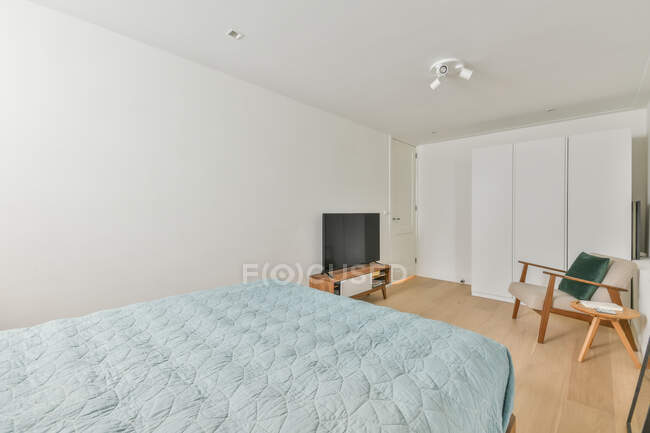 Moderno interno di piccola camera da letto con comodo letto e televisore su armadio in legno vicino ad arco e armadio in cottage — Foto stock