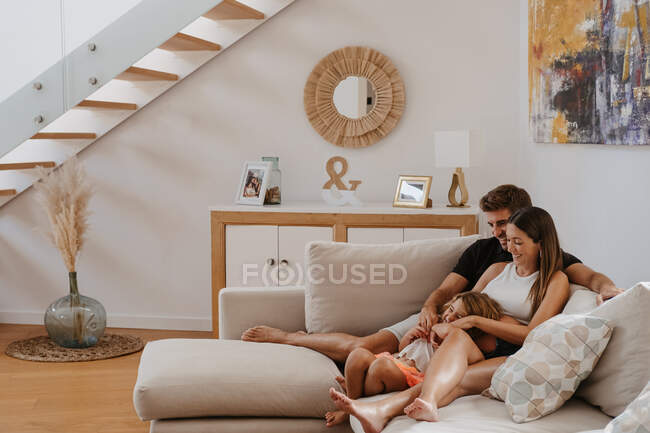 Carefree child playing with pregnant mother and smiling dad while resting on couch in living room — Stock Photo