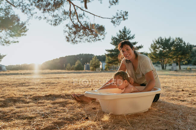 Smiling mom bathing toddler child while sitting on meadow under shiny sky on sunny day — Stock Photo
